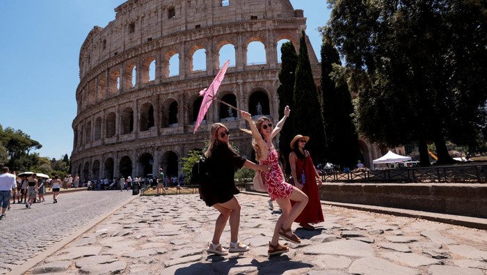'Neraka Bocor' di Roma, Wisatawan Kewalahan Tourists stand in front of a cooling fan installed outside the Colosseum in during the heatwave in Rome, Italy, June 30, 2025. REUTERS/Remo Casilli TPX IMAGES OF THE DAY