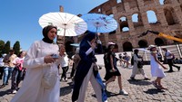 Wisatawan berjalan di bawah payung saat mengunjungi Colosseum di tengah gelombang panas musim panas di Roma, Italia, Senin (30/6/2025). Suhu di beberapa kota besar, termasuk Roma, melonjak hingga lebih dari 40 derajat Celsius. (REUTERS/Remo Casilli)  