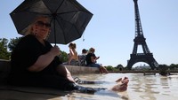 Sejumlah turis menyejukkan diri di Air Mancur Trocadero di sebelah Menara Eiffel saat gelombang panas awal musim panas melanda Paris, Prancis, Selasa (1/7/2025). Foto: REUTERS/Tom Nicholson