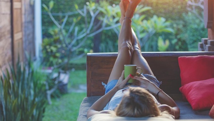 Girl enjoying early morning coffee on the garden sofa.
