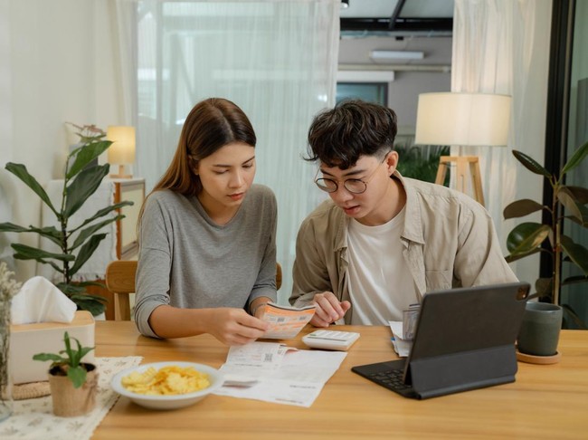 Ilustrasi pasangan merencanakan keuangan Happy young couple using laptop pay bills online in app calculate investment payment budget discuss finances at home.