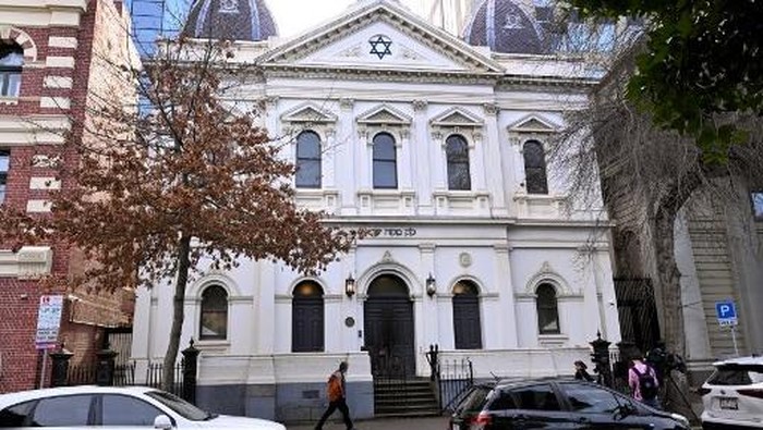 People pass the burnt front entrance of the East Melbourne Synagogue in Melbourne on July 6, 2025. A man suspected of setting fire to an Australian synagogue as worshippers ate dinner inside has been arrested and charged, police said on July 6. (Photo by William WEST / AFP)