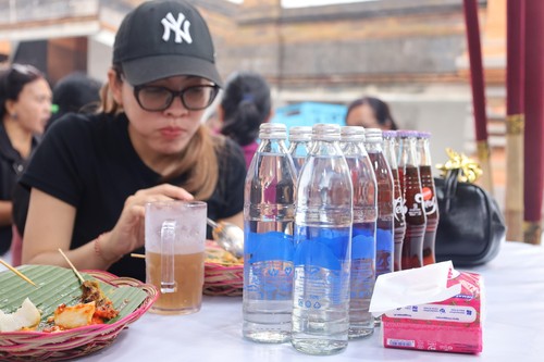 Pengunjung PKB di Art Center, Denpasar, tengah menikmati kuliner di samping pajangan air mineral berbotol kaca, Minggu (6/7/2025). (Aryo Mahendro/detikBali)