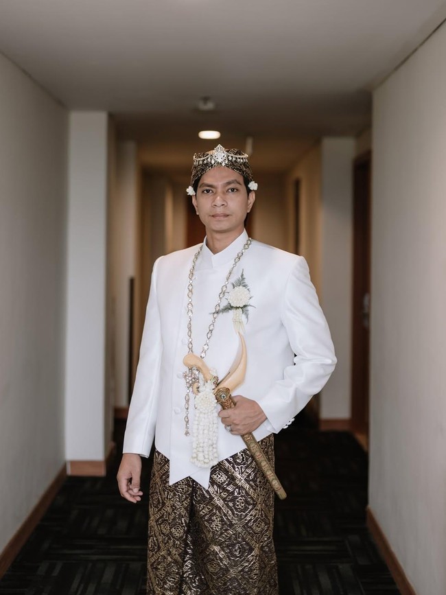 Adapun Dio Novandra, yang merupakan warga Medokan, Rungkut Surabaya, memakai beskap putih berpadu batik motif klasik. Tidak ketinggalan blangkon, dan keris sebagai aksesori pelengkap. (Foto: Instagram/@estoria_photography)