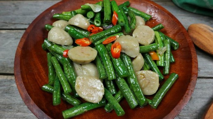 Indonesian food stir fry long bean or tumis kacang panjang and meatballs. Served on a wooden plate and isolated on grey background