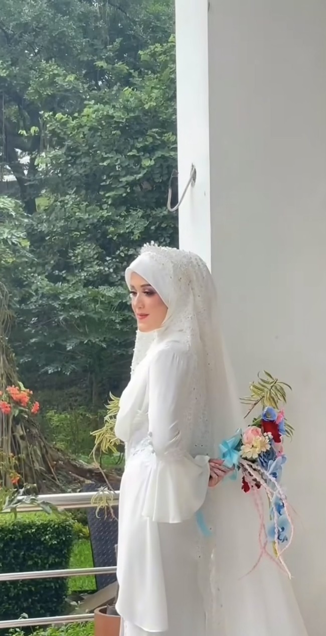 Alya tampil anggun dengan busana pengantin putih berhijab. Gaun yang dikenakannya itu memiliki lengan berbentuk flare sleeves yang memberikan kesan feminin. Penampilannya lengkap dengan hijab putih polos yang dilapisi veil panjang berhias payet. Foto: Instagram/@gunawandwicahyo13