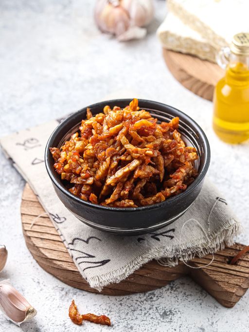 Dry tempeh (kering tempe), a typical Indonesian dish as a side dish for the main side dish. served in a bowl on a wooden cutting board on a white background