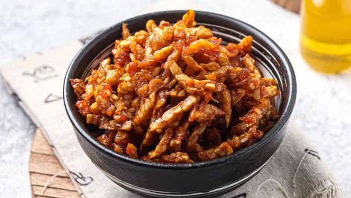 Dry tempeh (kering tempe), a typical Indonesian dish as a side dish for the main side dish. served in a bowl on a wooden cutting board on a white background