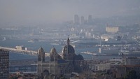 Asap tebal membubung di langit Marseille, kota terbesar kedua Prancis, saat kebakaran hutan menjalar hingga pinggir kota pada Selasa (8/7/2025), menyelimuti area pelabuhan dan pusat kota. (REUTERS/Alexandre Dimou)  