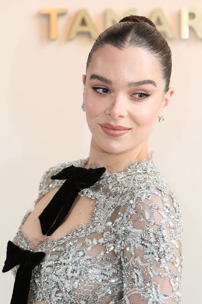 Rambut Hailee ditata sleek dengan disisir rapat ke belakang dan dsanggulchignon yang elegan. Makeup-nya menonjolkan alis tegas dan pulasan lipstik matte yang membuat wajahnya semakin terlihat tegas namun tetap glamor. Foto: Getty Images/Lyvans Boolaky,Jacopo Raule,Antoine Flament