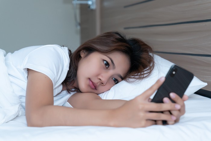 Young asian women lying in bed texting and checking social apps in smartphone on bed before after she sleeping at night. Mobile addict concept.