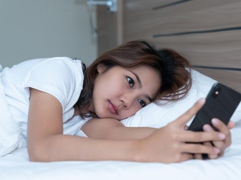 Ilustrasi bangun tidur langsung buka HP Young asian women lying in bed texting and checking social apps in smartphone on bed before after she sleeping at night. Mobile addict concept.