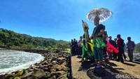 Pasangan nelayan simbolik berdiri di bibir dermaga yang langsung menghadap laut selatan. Aura dan Gilang berdiri tenang di tengah kerumunan, menyampaikan doa sebelum tabur bunga, persis di atas proyek yang sejak dulu tak selesai.