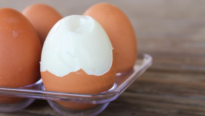 close up Six brown eggs in plastic box on bamboo table with one broken boiled egg.