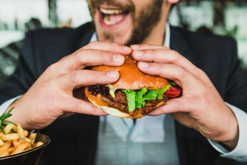 Pria sedang makan burger, makanan cepat saji