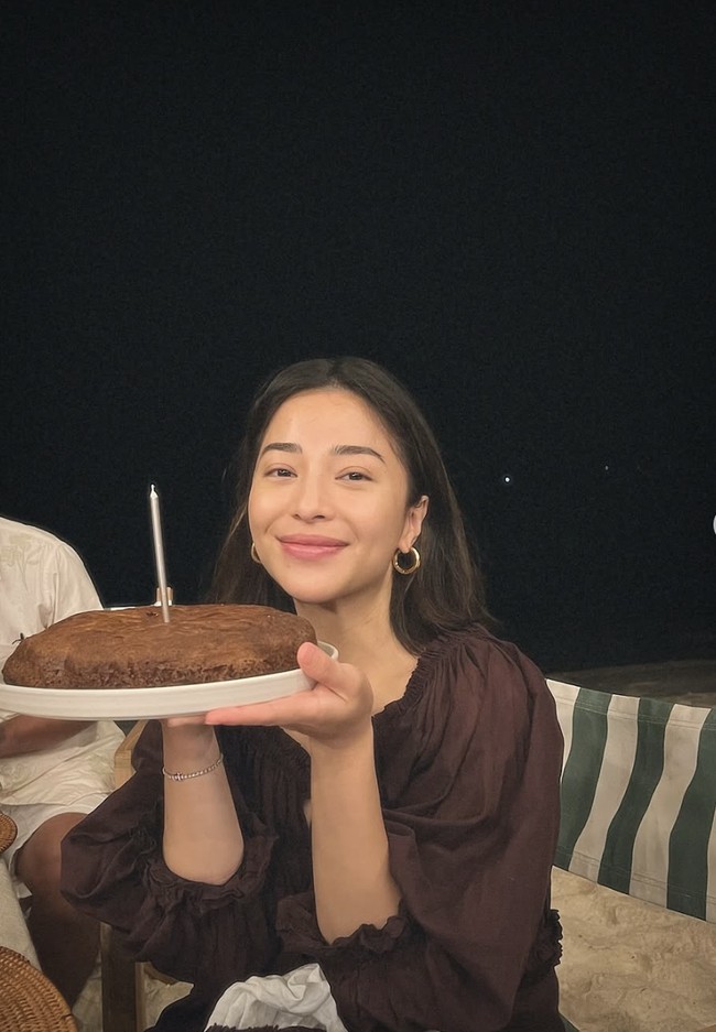 Di momen lain, Niki tampil beda dengan puffy dress merah maroon. Tanpa polesan makeup, ia tersenyum hangat sambil membawa kue. Foto: dok. Instagram @nikitawillyofficial94