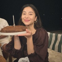 Di momen lain, Niki tampil beda dengan puffy dress merah maroon. Tanpa polesan makeup, ia tersenyum hangat sambil membawa kue. Foto: dok. Instagram @nikitawillyofficial94