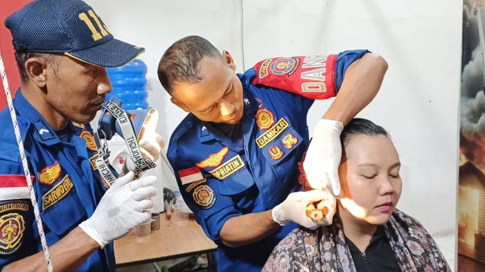 Petugas damkar saat membantu wanita melepaskan anting berkarat di telinganya.