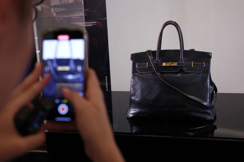 A cameraman films the Original Birkin, the handbag crafted by French luxury fashion house Hermes for artist Jane Birkin and offered to her in 1985, displayed during a media preview of Sotheby's Paris Fashion Icons Sale at Sotheby's auction house in Paris, France, July 2, 2025. REUTERS/Tom Nicholson