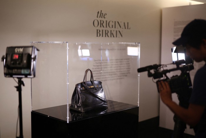 Tas Hermes Birkin Pertama Milik Jane Birkin Laris Dilelang A cameraman films the Original Birkin, the handbag crafted by French luxury fashion house Hermes for artist Jane Birkin and offered to her in 1985, displayed during a media preview of Sothebys Paris Fashion Icons Sale at Sothebyβs auction house in Paris, France, July 2, 2025. REUTERS/Tom Nicholson