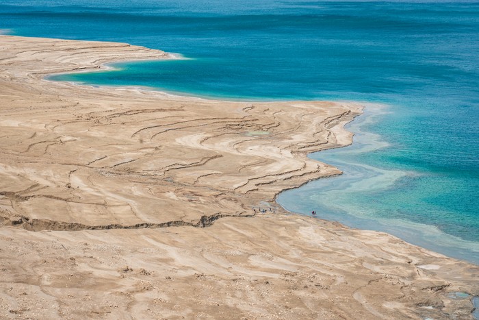 Laut Mati Scenic view from above along the dry rocky Dead Sea Coast of the West Bank Israel. Tourist walking down the rocky coast to swim in the salty water of the Dead Sea. Dead Sea, Ein Gedi, Israel, Middle east.