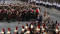 Presiden Prancis Emmanuel Macron berdiri di mobil komando bersama Kepala Staf Angkatan Bersenjata Prancis (CEMA) Thierry Burkhard. Bastille Day ini diawali Macron menaiki mobil taktis terbuka melewati Champs Elysées, Paris. Sepanjang jalan itu berbaris pasukan tentara memberi hormat kepada Macron. Foto: REUTERS/Gonzalo Fuentes