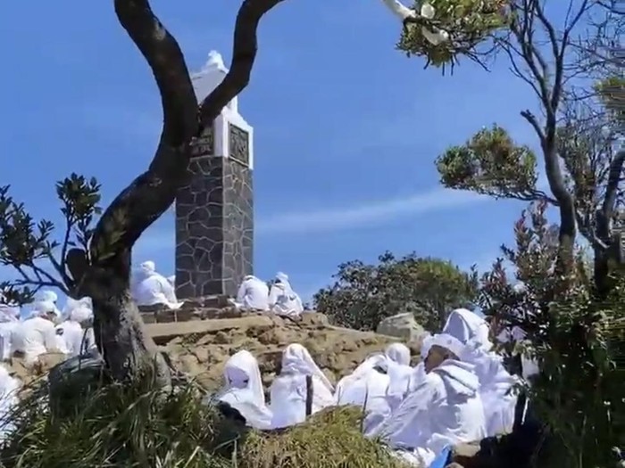 Sejumlah orang berbusana serba putih mengelilingi tugu di puncak Gunung Lawu Hargo Dumilah, Jumat (11/7/2025).
