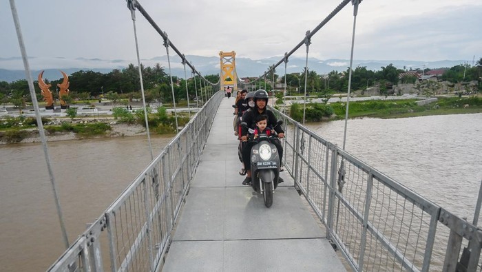 Pengendara sepeda motor dan pejalan kaki melintas di atas jembatan gantung yang baru dioperasikan di Desa Tinggede, Sigi, Sulawesi Tengah, Selasa (15/7/2025). Setelah dua kali ambruk akibat bencana pada 2015 silam, jembatan gantung dengan bentangan 115 meter yang menghubungkan Desa Tinggede dan Desa Kalukubula di Kabupaten Sigi dan hanya dapat dilewati pejalan kaki dan sepeda motor itu akhirnya difungsikan untuk umum setelah direkonstruksi. ANTARA FOTO/Basri Marzuki/bar