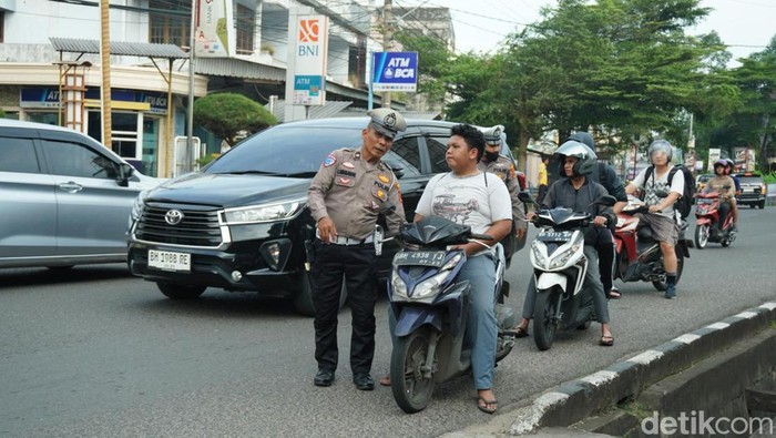 Polisi saat memberhentikan dan menilang pengendara motor tak berhelm.