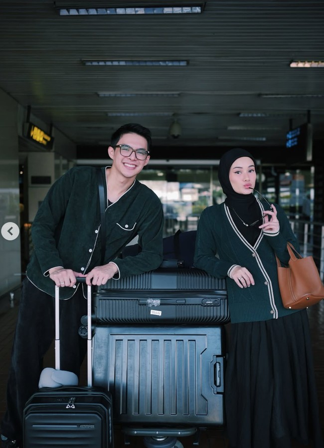 Dinda dan Rey tampil serasi di bandara dengan outfit travel bernuansa hitam dan hijau tua. Mereka mengenakan jaket matching dan membawa koper besar. Foto: Instagram/@rey_mbayang