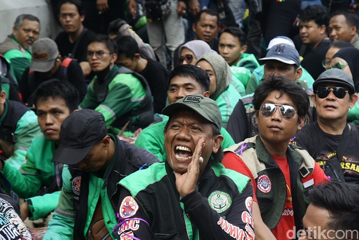 Ratusan ojol gelar demo di Monas, Kamis (17/7), menolak status buruh dan potongan 10%, serta mendesak Perppu sebagai payung hukum layanan ojol.