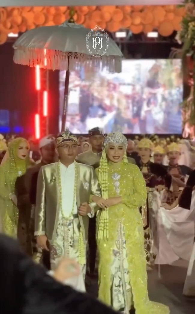 Di acara resepsi Maulana mengenakan beskap berwarna gold muda dengan kain batik motif parang dan flora sebagai bawahannya. Kepala mempelai pria dihiasi blangkon batik. Sementara Putri tampil dengan kebaya modern bernuansa hijau keemasan lengkap dengan Siger di kepalanya. Foto: Instagram/@putri.karlina14
