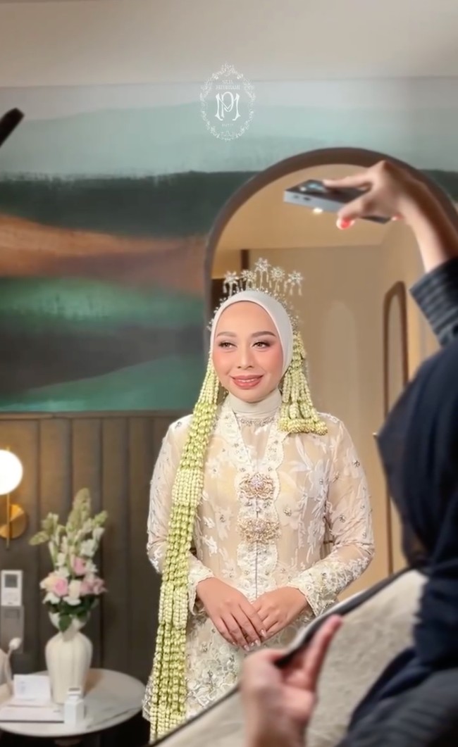 Penampilannya kian lengkap dengan hijab serasi dengan kebaya, dan dipercantik dengan sanggul ronce melati yang menjuntai panjang di kedua sisi. Juga terdapat bros besar di dada yang menambah kesan tradisional dan berkelas. Foto: Instagram/@putri.karlina14