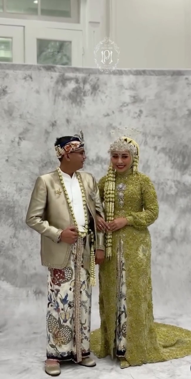 Di acara resepsi Maulana mengenakan beskap berwarna gold muda dengan kain batik motif parang dan flora sebagai bawahannya. Kepala mempelai pria dihiasi blangkon batik, pelengkap penampilan keseluruhan yang memperkuat nuansa budaya. Foto: Instagram/@putri.karlina14
