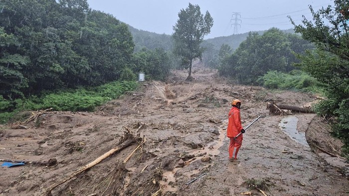 This handout photo taken on July 19, 2025 and released by Gyeongsangnam-do Fire Department via Yonhap shows a rescue member standing on a mud-covered road after a landslide hit a village in southern Sancheong county as heavy rain continued to pound the country. A landslide triggered by torrential rain killed at least one person in South Korea, the national fire agency said on July 19. (Photo by Handout / Gyeongsangnam-do Fire Department / AFP) / - South Korea OUT / RESTRICTED TO EDITORIAL USE - MANDATORY CREDIT 