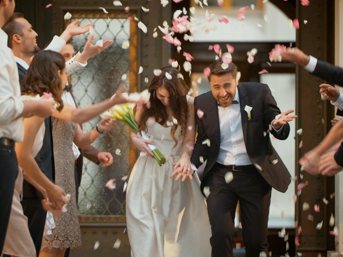 629568186. Friends throwing flower petals over bride and groom as they leave church.