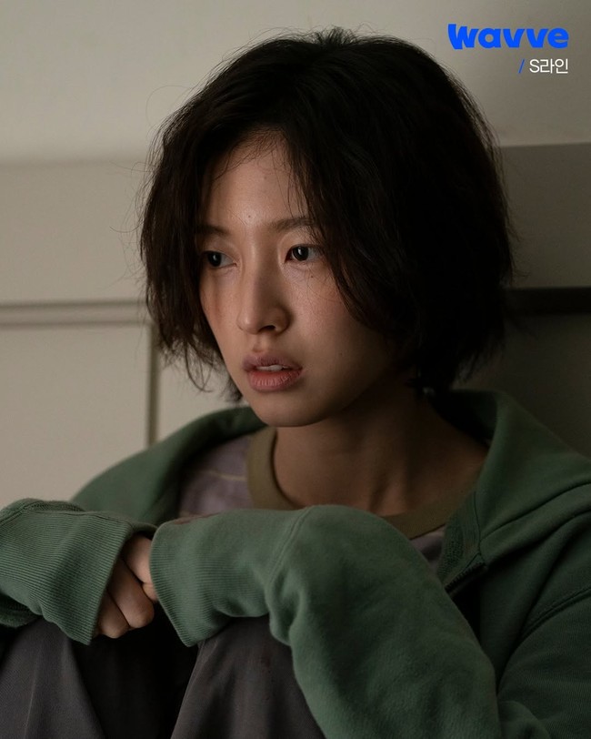 Drama Korea S Line menampilkan sisi baru Arin Oh My Girl sebagai Shin Hyun Seup. Ia muncul sebagai siswi SMA yang dihantui trauma, memiliki potongan rambut pendek acak-acakan, hampir tanpa riasan dan ekspresi wajah suram. Foto: dok. Wavve