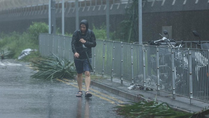 Topan Wipha melanda wilayah Hong Kong pada Minggu (20/7/2025), disertai hujan deras dan angin kencang yang memaksa aktivitas kota nyaris lumpuh. Sejumlah pohon tumbang menutup jalanan, sementara pejalan kaki terpaksa berjalan tertatih di tengah badai, berusaha melindungi diri dengan payung yang tak mampu menahan kuatnya tiupan angin. REUTERS/Tyrone Siu