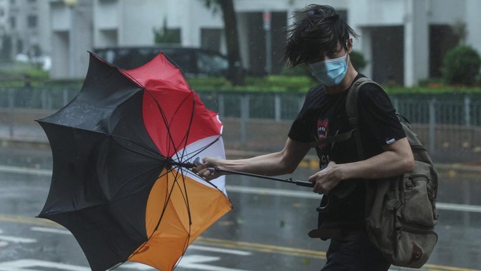 Topan Wipha melanda wilayah Hong Kong pada Minggu (20/7/2025), disertai hujan deras dan angin kencang yang memaksa aktivitas kota nyaris lumpuh. Sejumlah pohon tumbang menutup jalanan, sementara pejalan kaki terpaksa berjalan tertatih di tengah badai, berusaha melindungi diri dengan payung yang tak mampu menahan kuatnya tiupan angin. REUTERS/Tyrone Siu