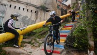 Aksi peserta saat mengendalikan sepedanya di jalur sempit dan menurun di permukiman padat penduduk Petare yang menantang adrenalin. Petare dikenal sebagai salah satu lingkungan terbesar dan tersibuk di Amerika Latin, dengan gang-gang sempit, tangga curam, dan belokan tajam—yang justru menjadi lintasan balapan. Foto: REUTERS/Gaby Oraa