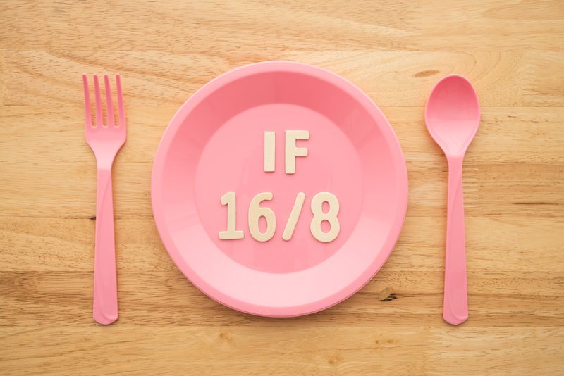 IF (Intermittent Fasting) 16 and 8 diet rule and weight loss concept. IF 16 and 8 letter on pink plate, spoon and fork on wooden table background.