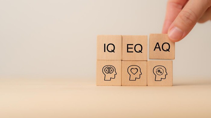 Wooden blocks with the letters IQ, EQ and AQ representing Intelligence Quotient, Emotional Quotient, Adaptability Quotient. A hand adjusting AQ block, symbolizing adaptability in modern intelligence.