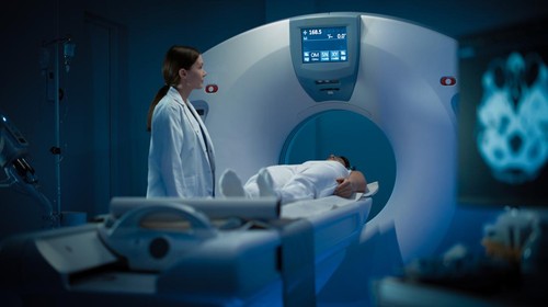 In Medical Laboratory Radiologist Controls MRI or CT or PET Scan with Female Patient Undergoing Procedure. High-Tech Modern Medical Equipment. Friendly Doctor Chats with Patient