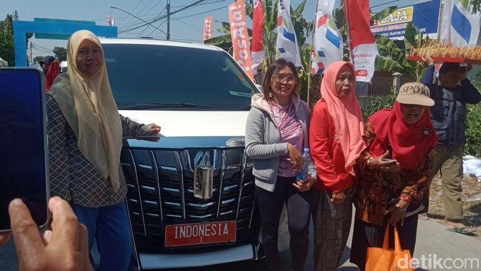 Momen warga berfoto di samping Alphard putih berpelat Indonesia 1 saat peluncuran Kopdes Merah Putih di Bentangan, Wonosari, Klaten, Minggu (21/7/2025).