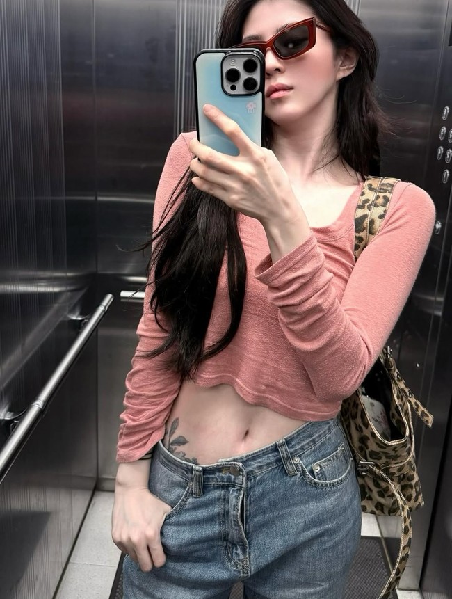 Saat mirror selfie di lift, Han So Hee menunjukkan sisi rebel dengan tato ukiran bunga di bawah perutnya. Tato tersebut terlihat jelas karena pilihan low-rise jeans dan crop top pink yang dikenakannya. Foto: dok. Instagram @xeesoxee