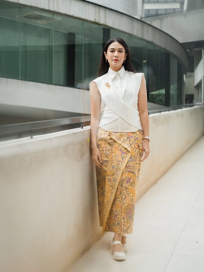 Dian Sastrowardoyo menampilkan kebaya modern yang sleek dan tegas. Potongan sleeveless dengan kerah kemeja dan siluet asimetris menciptakan nuansa kontemporer. Kain batik sogan bernuansa kuning emas menjadi pelengkap yang tetap menjaga akar tradisional dalam balutan modernitas. Foto: Instagram/@theraldisastr