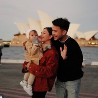 Jessica Mila terlihat berpose bahagia bersama suami dan buah hatinya dengan latar belakang Sydney Opera House. Momen ini memperlihatkan kehangatan keluarga kecil mereka saat menikmati senja di tepi laut. Foto: Instagram/@jscmila
