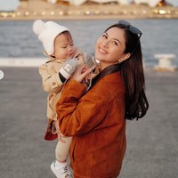 Saat momong sang buah hati, Jessica mengenakan jaket cokelat berbahan suede dipadukan dengan celana hitam. Sang anak juga tampil lucu dengan jaket beige, topi rajut putih, dan sarung tangan. Foto: Instagram/@jscmila