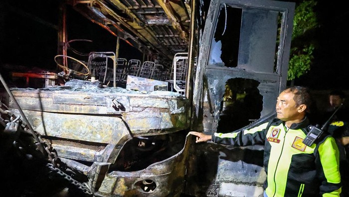 Petugas kepolisian mengamati kondisi bangkai bus pascakebakaran di ruas jalan nasional Nganjuk, Jawa Timur, Selasa (22/7/2025). Kecelakaan lalu lintas yang melibatkan  bus antar kota dalam provinsi (AKDP) rute Surabaya-Ponorogo dengan sepeda motor itu menyebabkan bus terbakar dan satu orang meninggal dunia. ANTARA FOTO/Muhammad Mada/nz