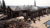 Puing-puing rumah terlihat di tengah asap dan bara, menandai dahsyatnya kebakaran hutan di desa Souni. REUTERS/Yiannis Kourtoglou
